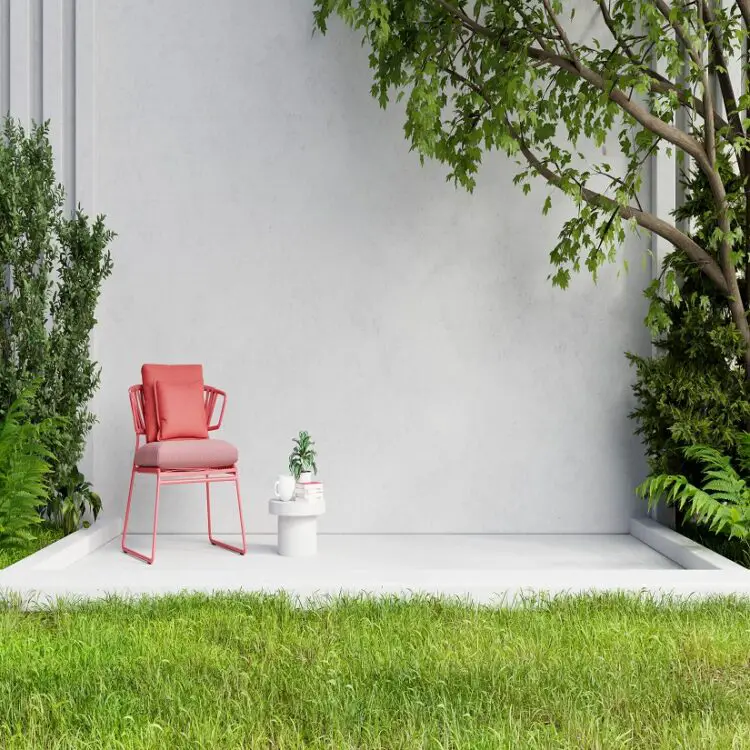 A red chair in front of a white wall in a garden.
