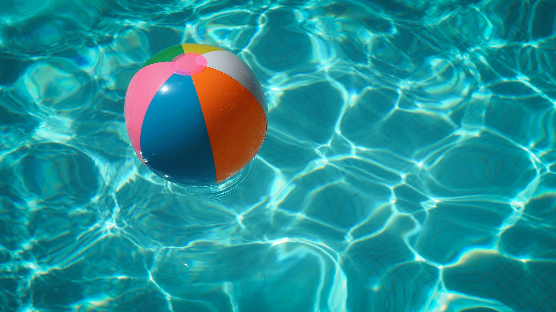 A colorful beach ball floating in a backyard pool.