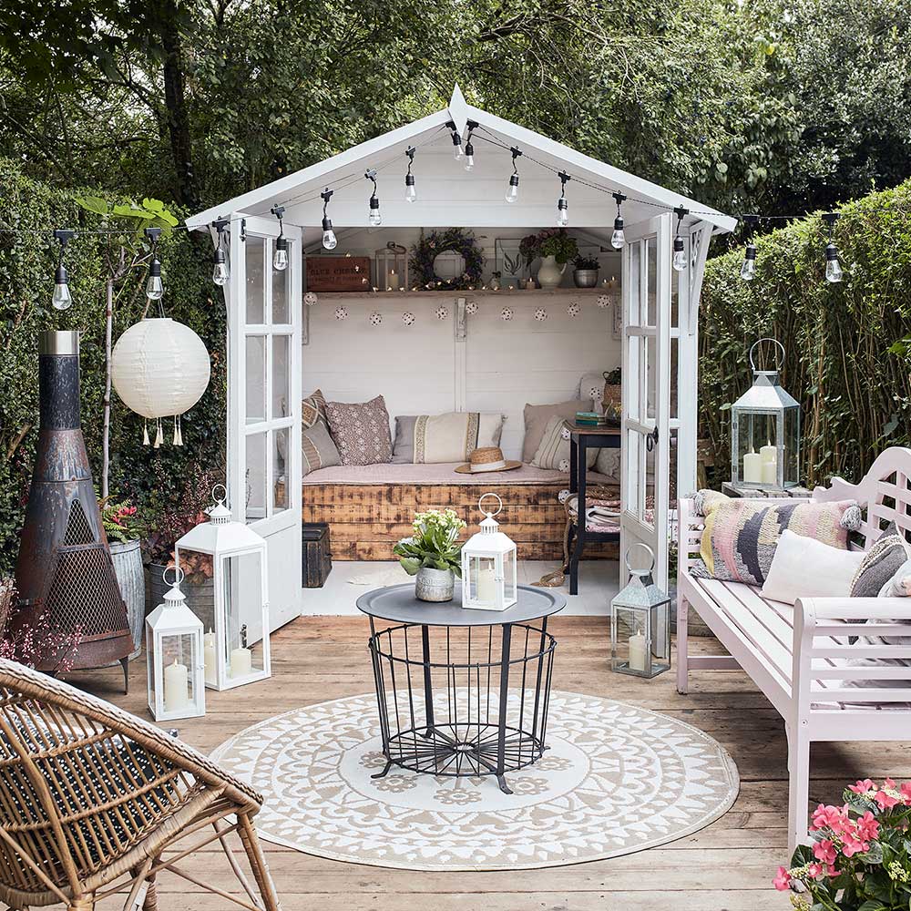 A she-shed featuring a white garden shed with wicker furniture.
