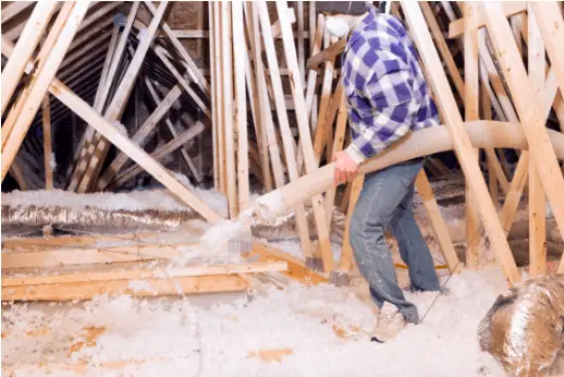 A man using a hose to apply spray foam insulation in an attic.