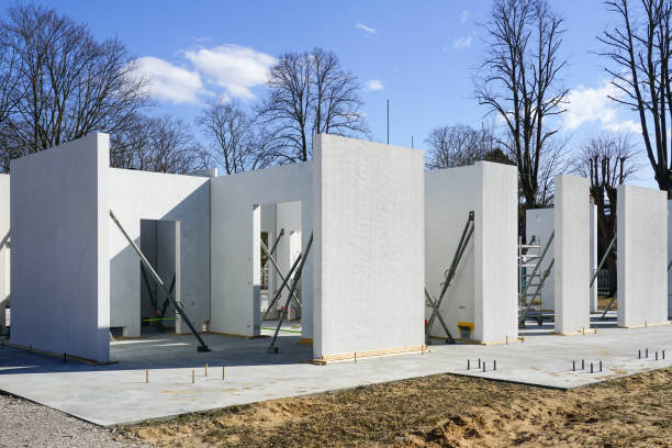 A white house under construction with concrete panels in a wooded area.