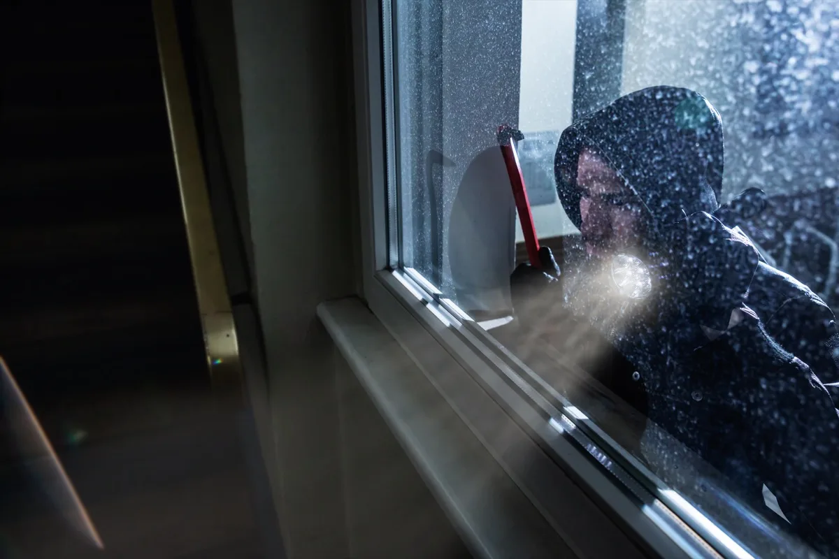 A man in a hoodie enhancing home security with a flashlight out of a window.