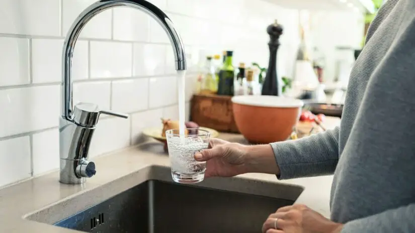 A man is holding a glass of water in front of a kitchen sink.