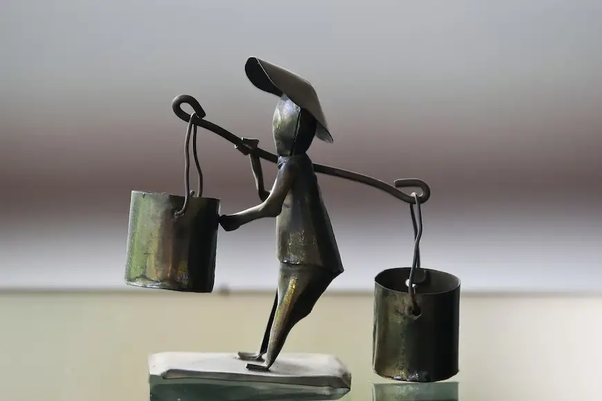 Metal sculpture of a man carrying a bucket.