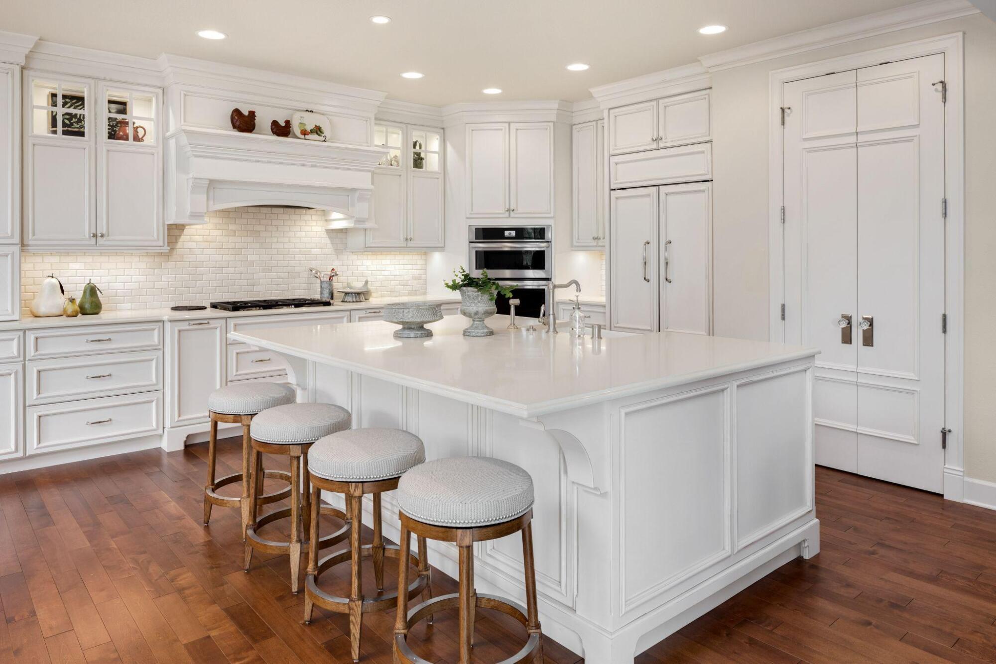 A white kitchen with a center island and stools designed for an organizational kitchen.