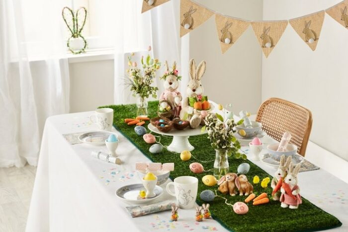 An Easter table decorated with bunnies, flowers, and artificial grass.
