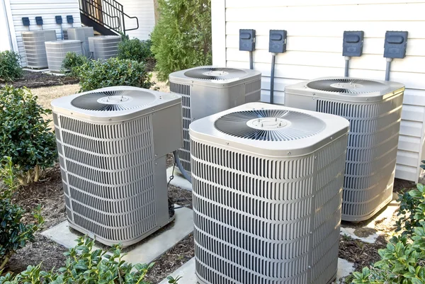 A group of air conditioning units in front of a house.