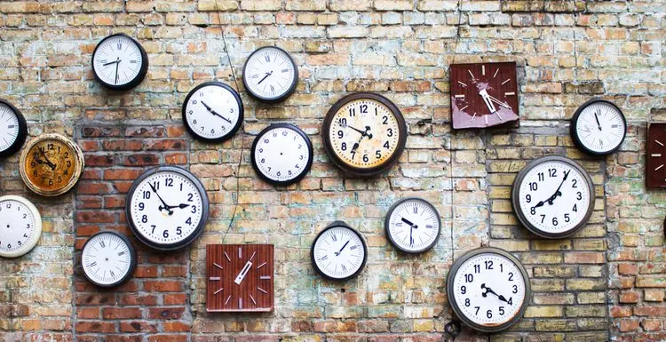 A variety of clocks on a brick wall display different types of wall clocks.