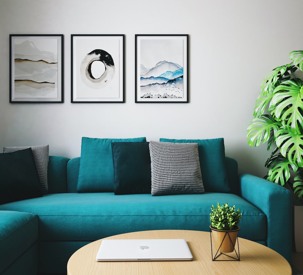 A living room with a teal couch and two framed pictures is the perfect space for buying a new sofa.