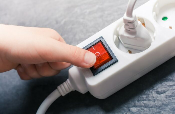 A hand pressing a red button on a power outlet demonstrates electrical safety.