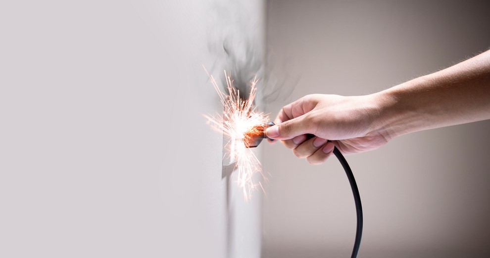 One way to improve electrical safety at home: A hand is holding a spark plug in front of a wall.