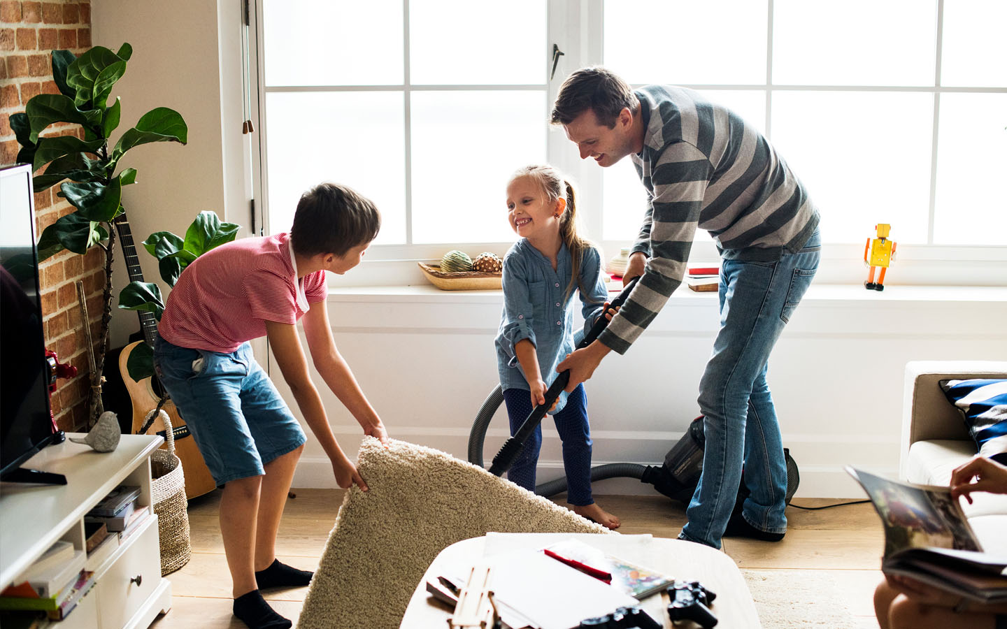 A man and two children making home maintenance mistakes while vacuuming a rug in a living room.
