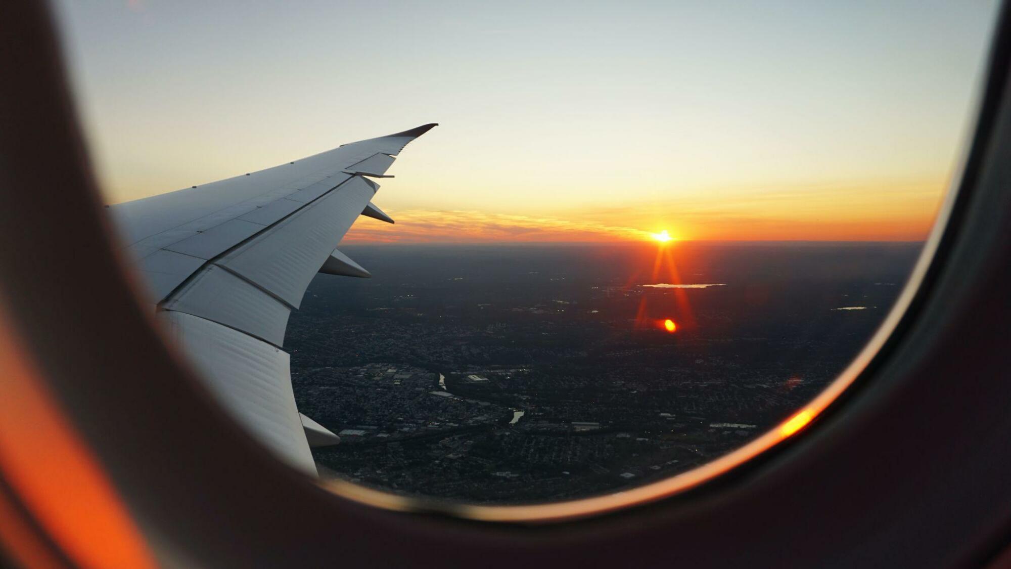Tips for travelers: An airplane wing is seen through a window at sunset.