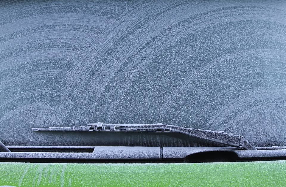 A green car with frost on the windshield and quality wipers.