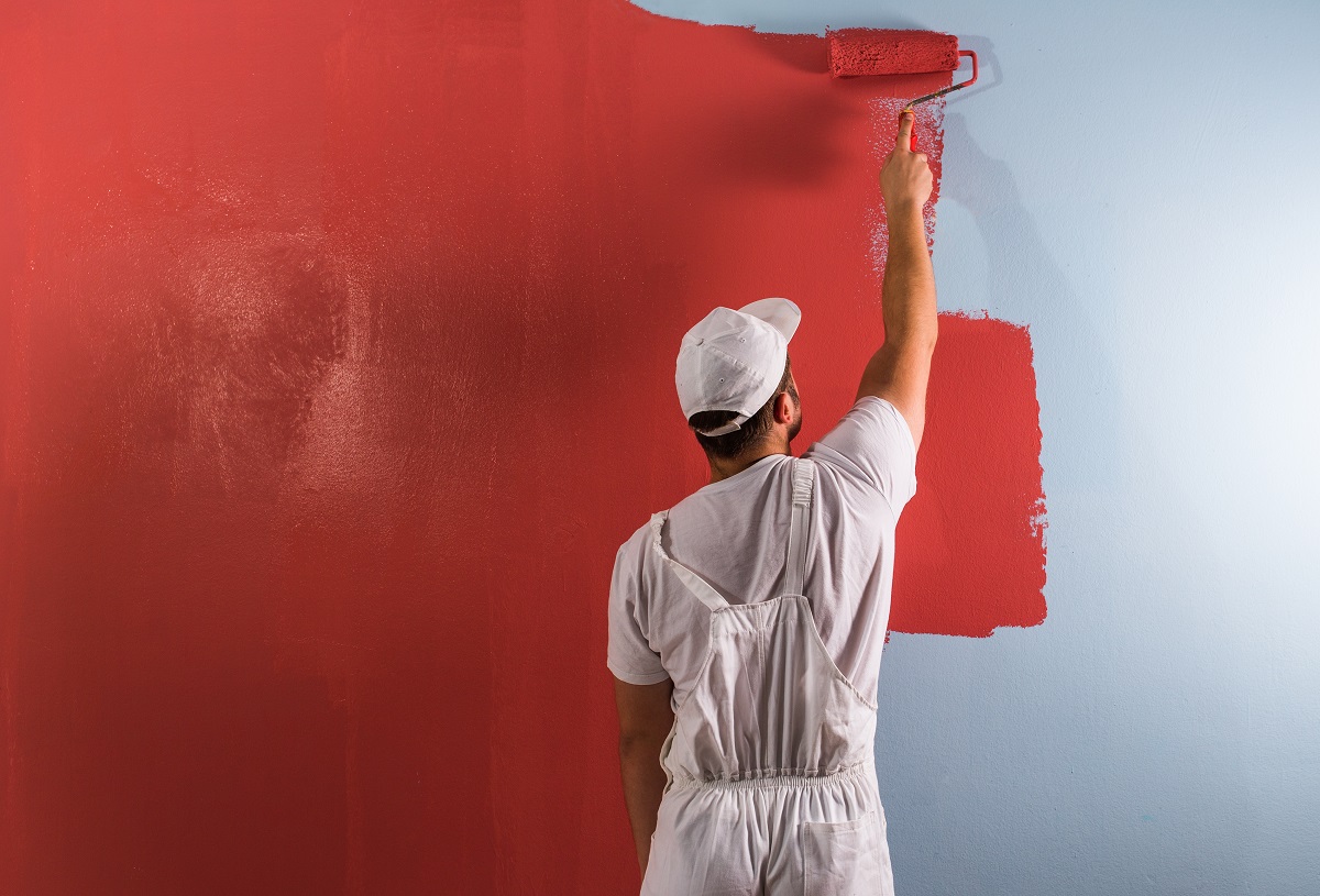 A man using a paint roller to hire painters for painting a red wall.