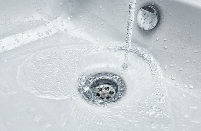 A close up of a sink with water coming out of it, examining the impact of smart water meters as a home investment.