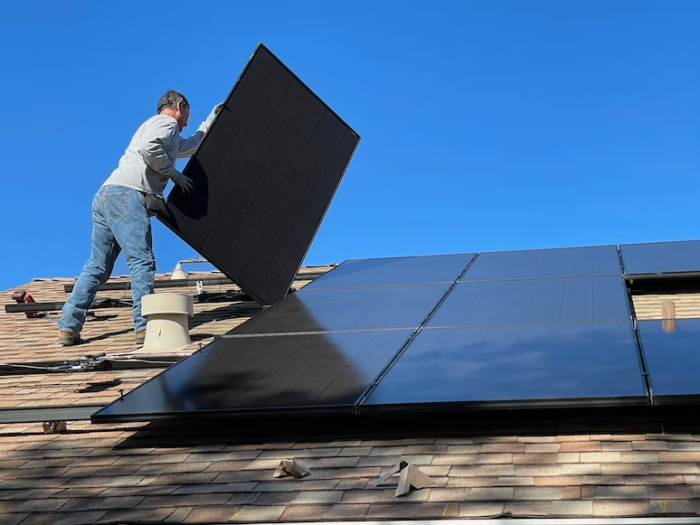 A man installing solar panels on an eco-friendly house roof.