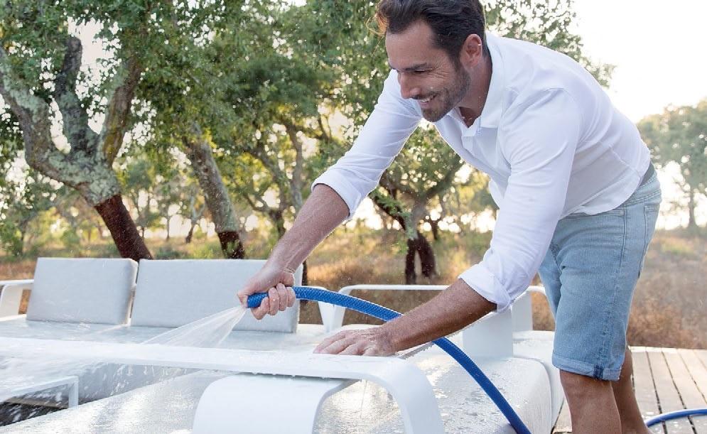 A man cleaning outdoor furniture with a hose.