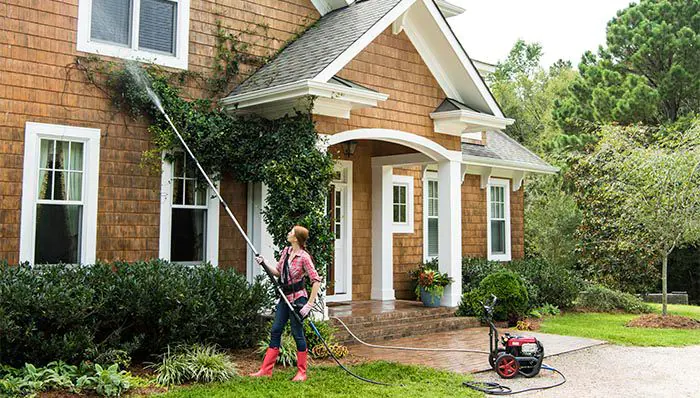 A woman pressure washes the front of a house.