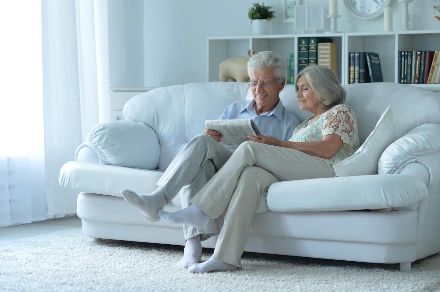 An elderly couple sitting on a white couch, enjoying a safe and comfortable retirement at home.