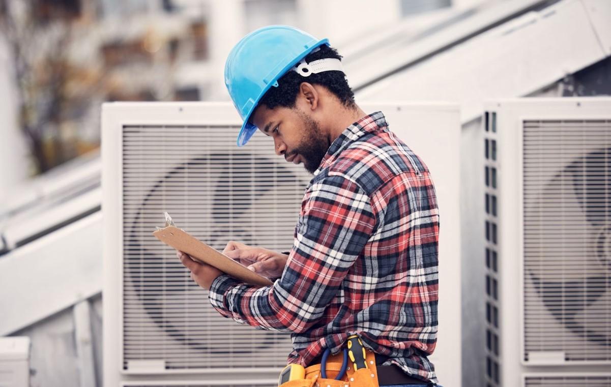 A man holding a clipboard in front of air conditioning units, estimating AC repair costs.