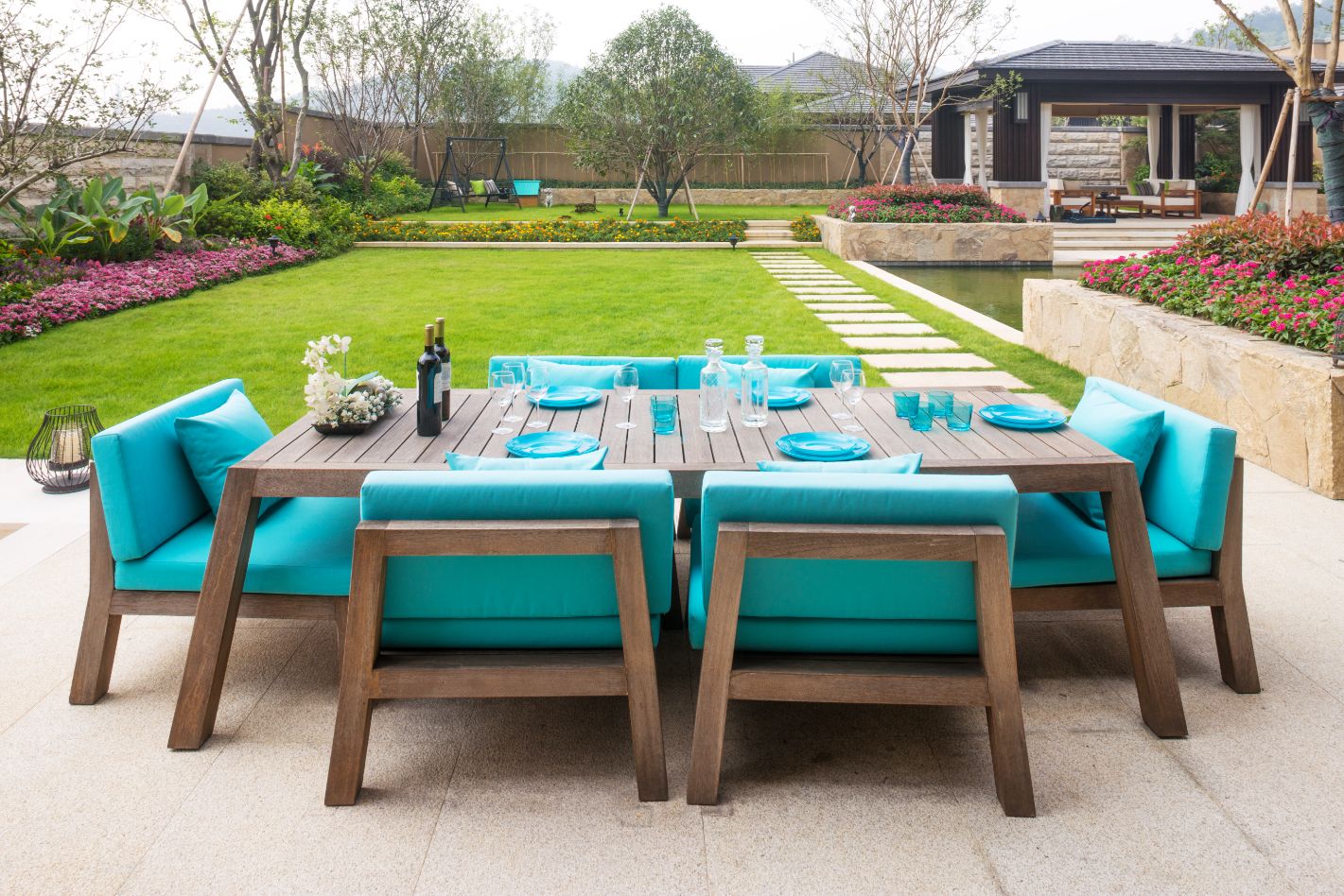 An outdoor dining table with blue chairs and a green lawn featuring the best wood furniture.