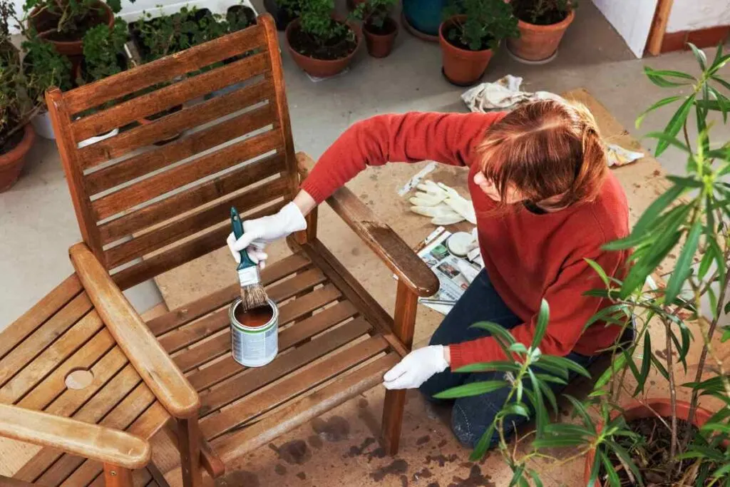 A woman painting a wooden chair in the garden, selecting the best outdoor furniture wood.