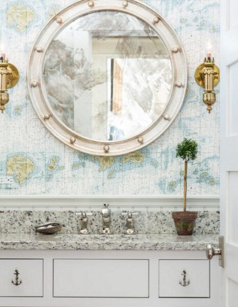 A bathroom with a round mirror decorated in nautical wallpaper.