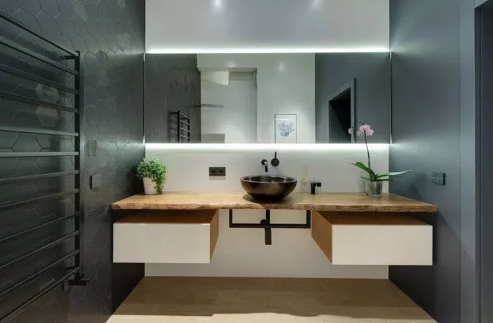 A modern bathroom with black and white walls, a wooden sink, and a decorated mirror.