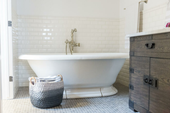 A white tiled French country bathroom with a white tub and basket.
