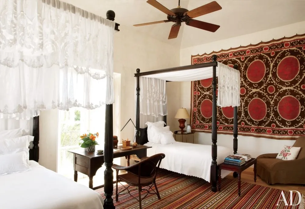 A boho-themed bedroom with a four poster bed and a fan.