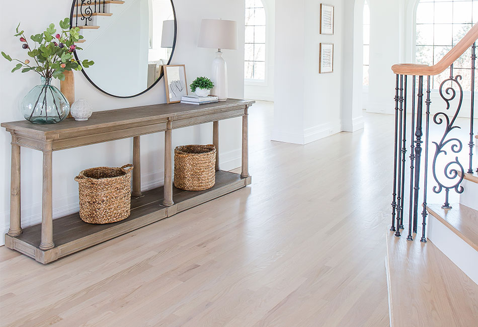 A hallway with white oak hardwood floors and a mirror.