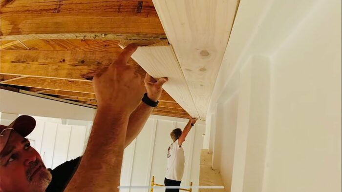 A man is installing tongue and groove wood beams on the ceiling.