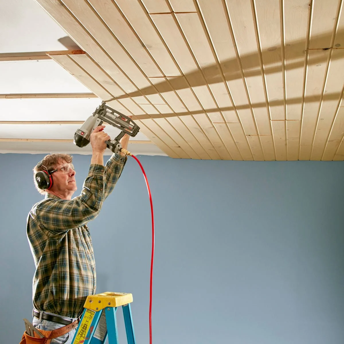 A man is installing tongue and groove on a ceiling in a room.