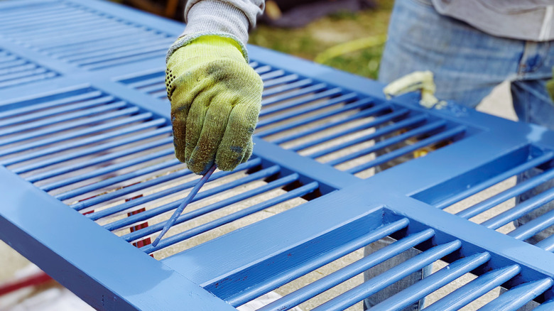 A person wearing gloves is painting a blue grate with vinyl paint.