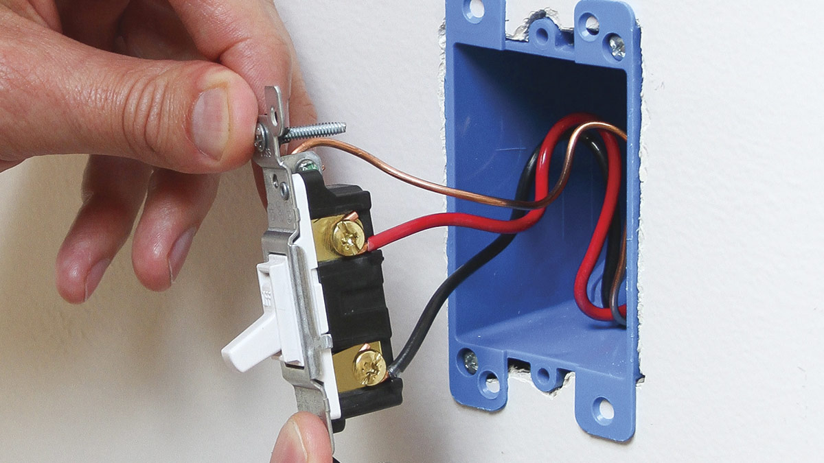 A person is installing a light switch on a wall, highlighting the advantages of switch loop wiring.