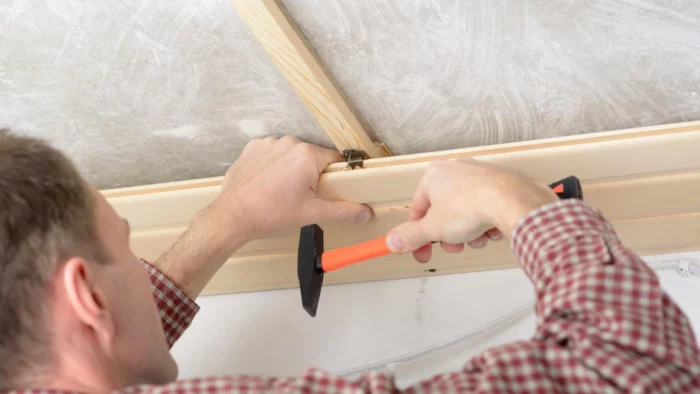 A man is hammering a tongue and groove into a ceiling.