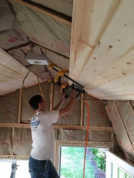 A man is installing tongue and groove panels on the ceiling of a house.