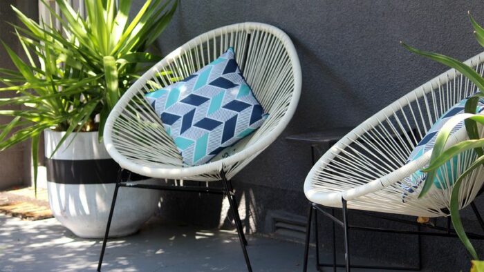 Two wicker accent chairs on a patio with a potted plant.