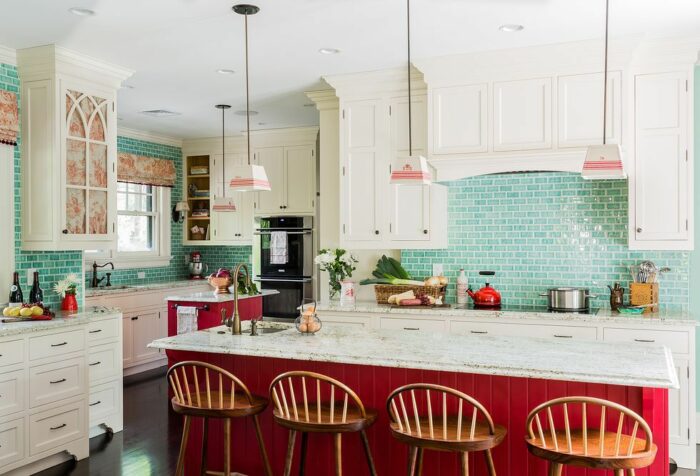 A kitchen with turquoise tile and red stools.