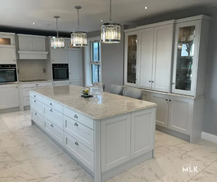 A kitchen with light gray cabinets and marble counter tops.