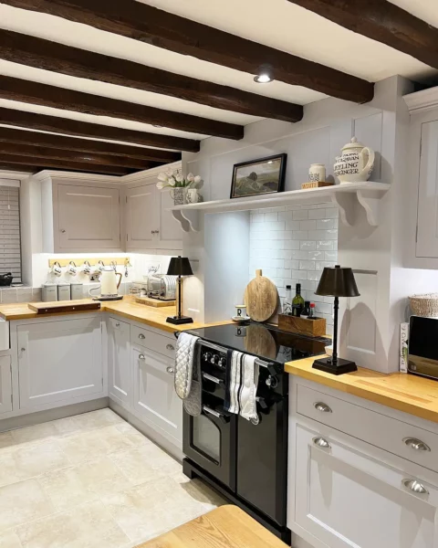 A kitchen with light gray cabinets and wooden beams.