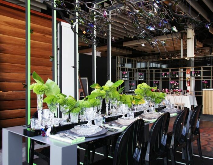 Design ideas for a restaurant table set up with green flowers and black chairs.