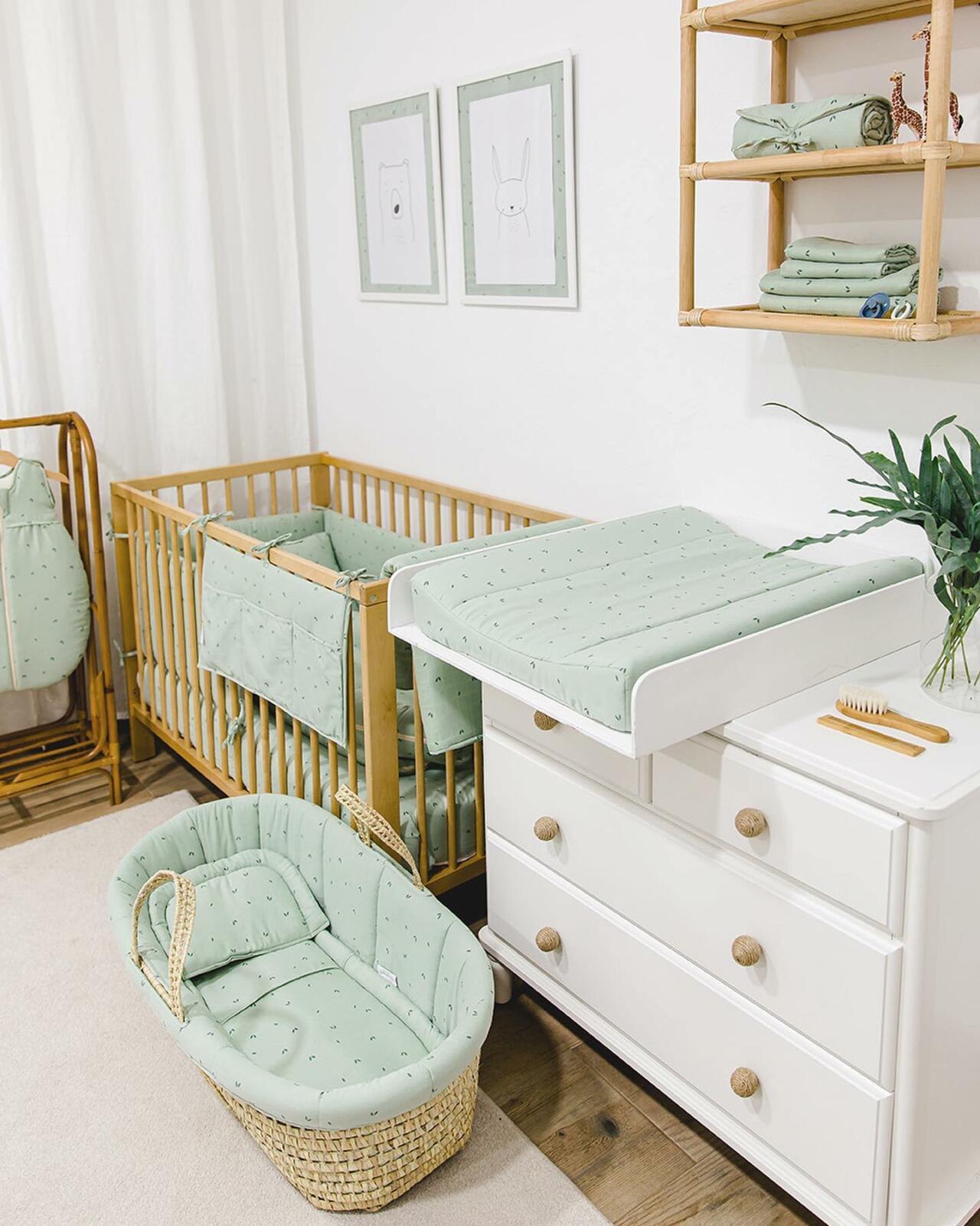 A sage green nursery with a crib, dresser, and wicker basket.
