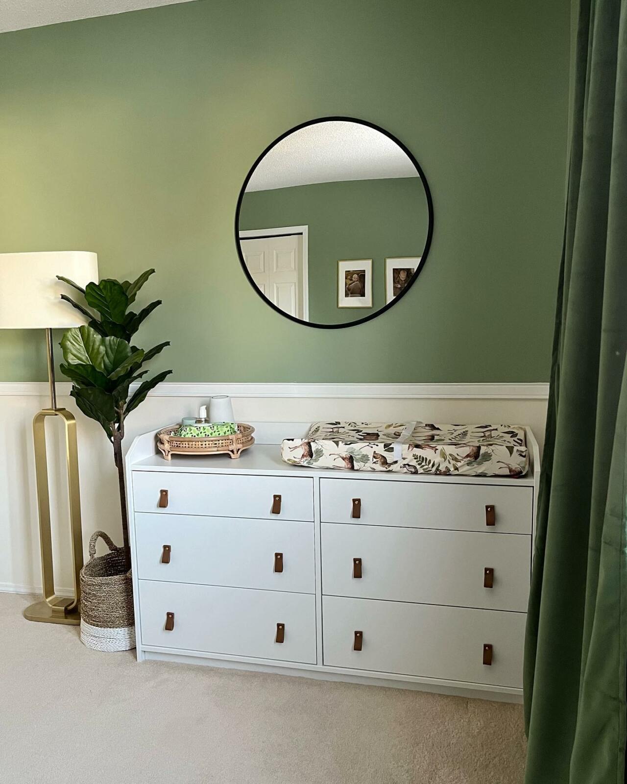 A sage green nursery with a white dresser.
