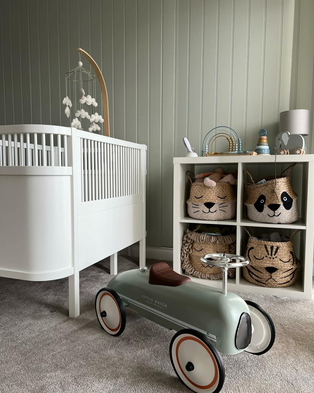 A sage green nursery with a crib and a toy car.
