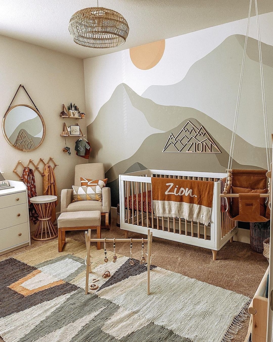 A sage green nursery with a mountain mural on the wall.