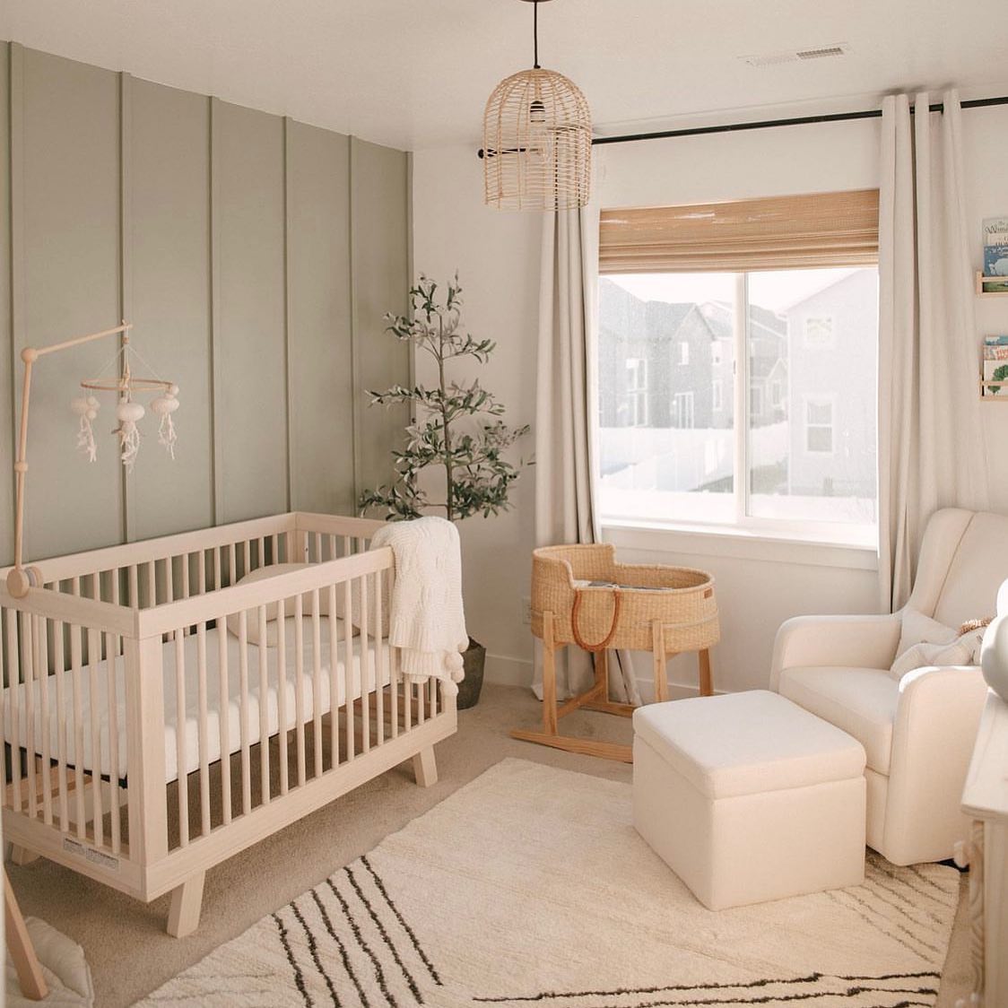 A sage green nursery with a crib, dresser, and chair.