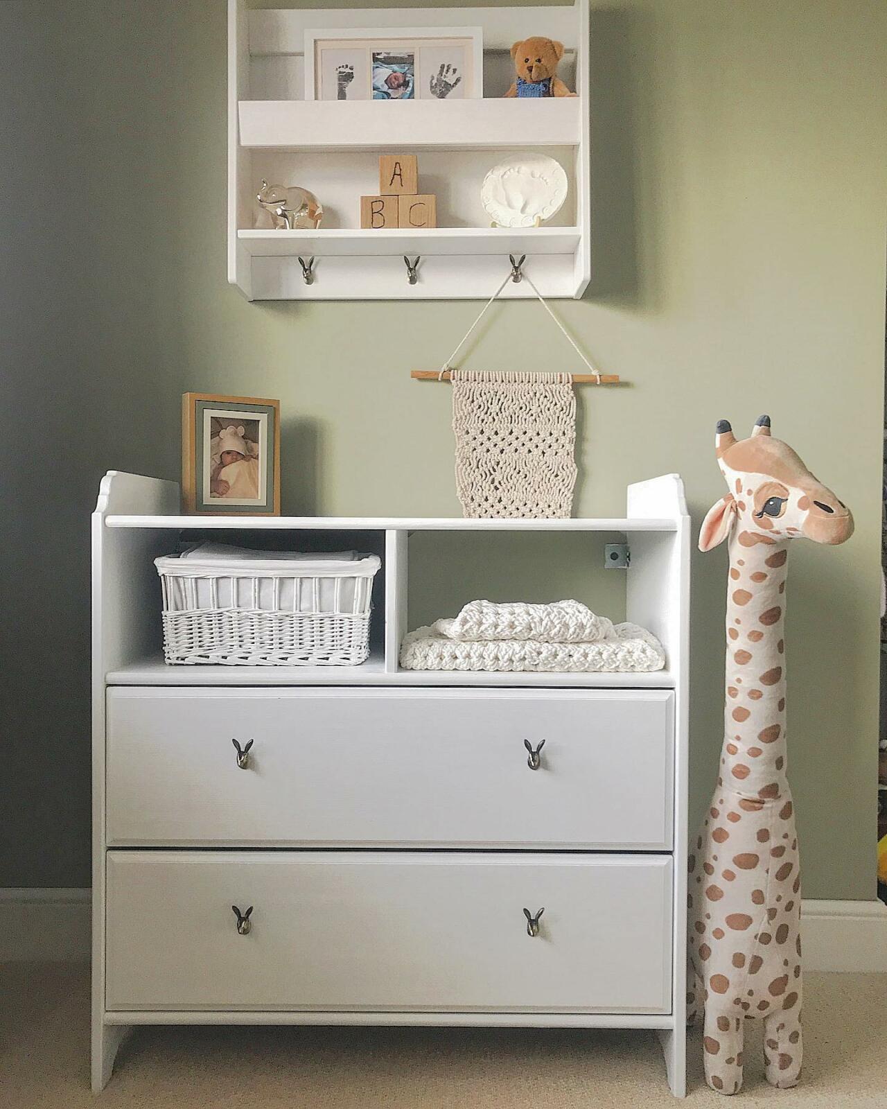 A sage green nursery with a white dresser featuring a giraffe on top.