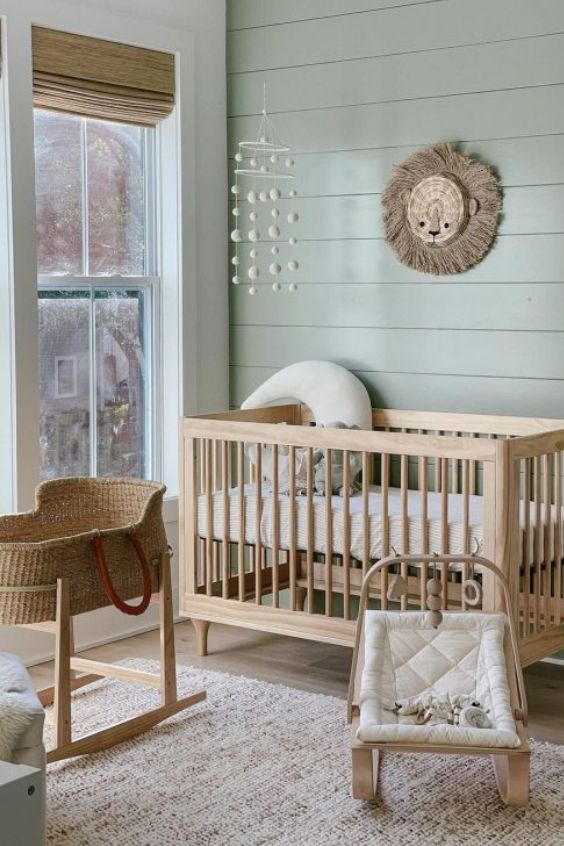 A sage green nursery with a crib, a rocking chair, and a wicker basket.